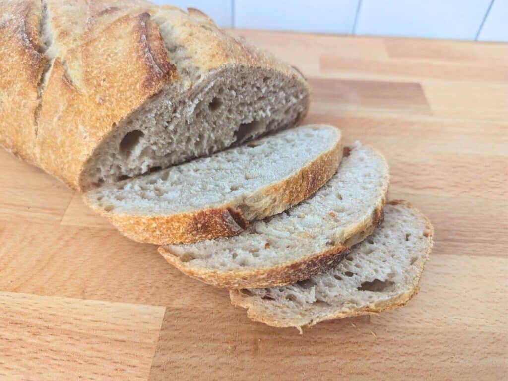 Image shows a Partially sliced loaf of sourdough bread on a wooden board.