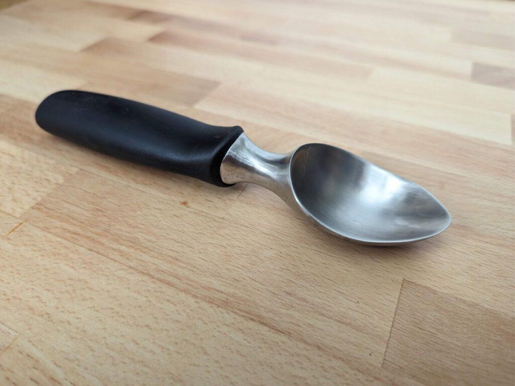Image shows an ice cream scoop lying on its side on a wooden table.