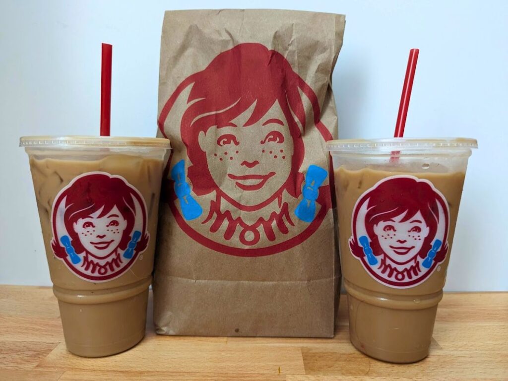 Image shows a Wendys breakfast bag and frosty cream cold brew on a wooden table.