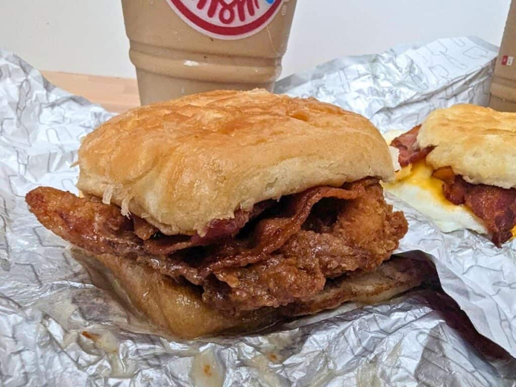Image shows a Wendys maple bacon chicken croissant on the Wendy's wrapper with a Frosty Cream cold brew behind it.