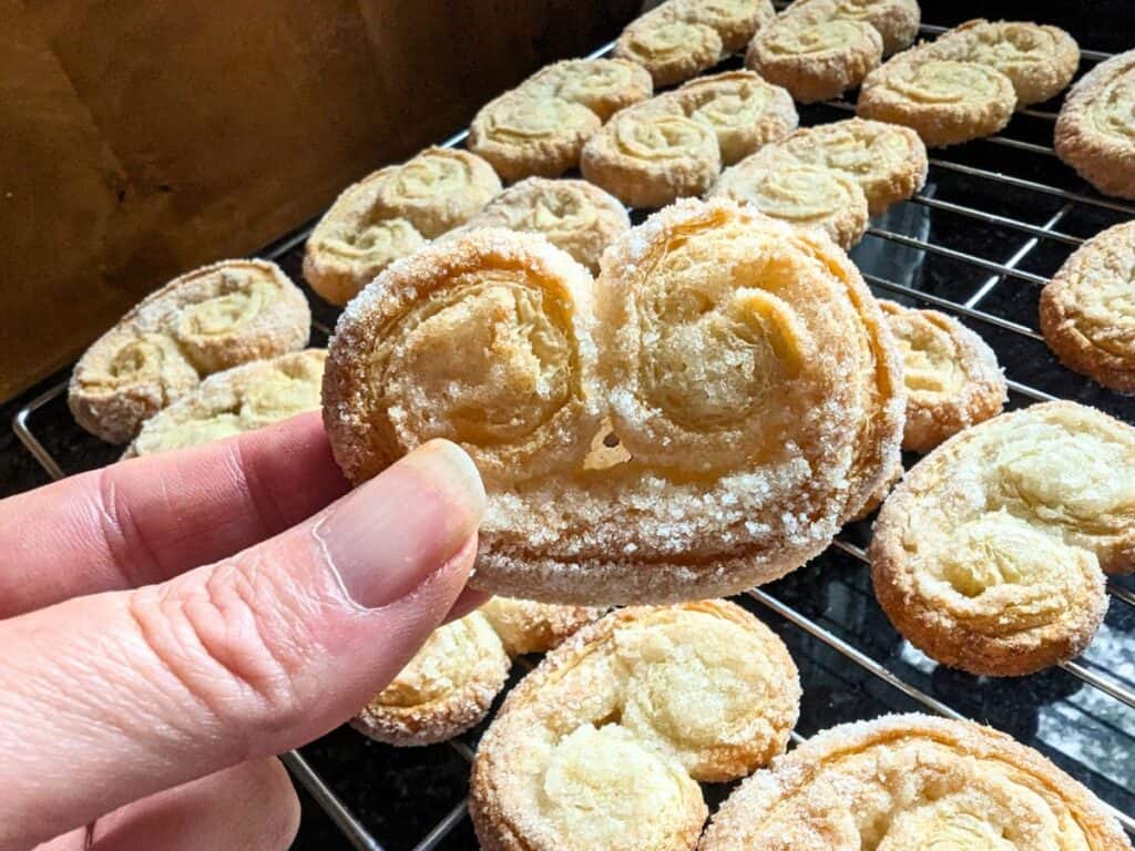 Image shows a Hand holding a palmier over a rack of more.