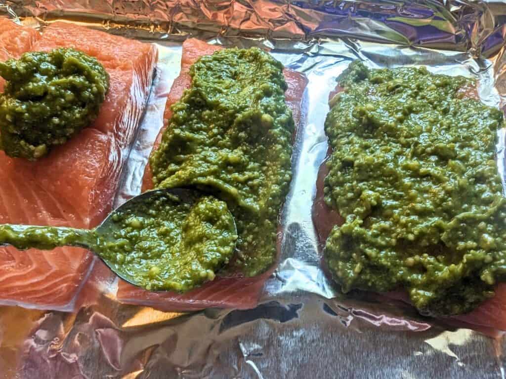 Image shows a spoon Adding pesto to salmon fillets.