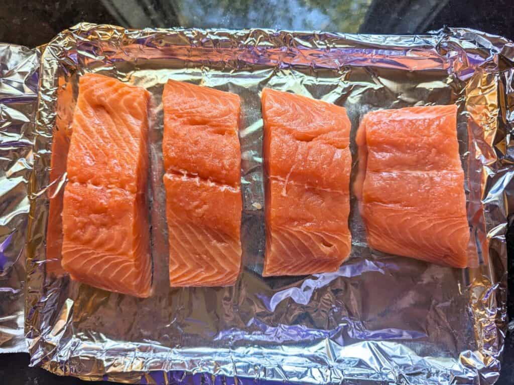 Image shows an Overhead of salmon fillets on a baking tray lined with tin foil.
