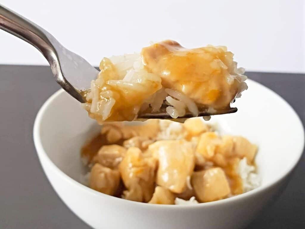 Image shows a fork holding a bite of homemade orange chicken.