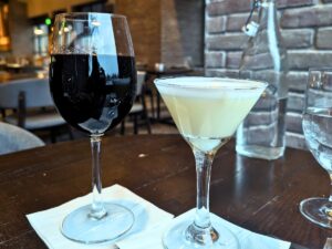 Image shows the Three Embers citrus flower sour and a glass of red wine on a table.