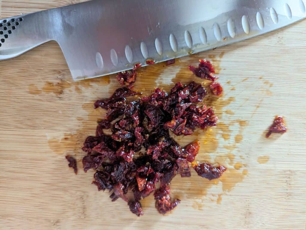 Image shows Chopped sundried tomatoes on a cutting board.