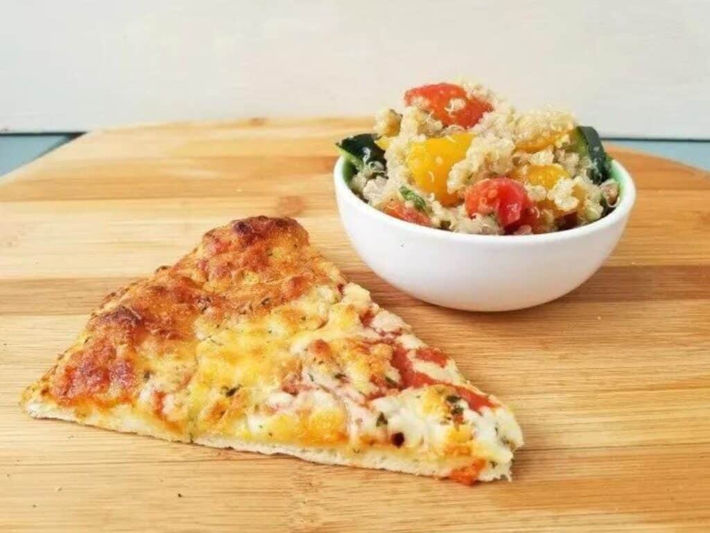 Image shows a bowl of delicious tomato quinoa salad with a slice of pizza.
