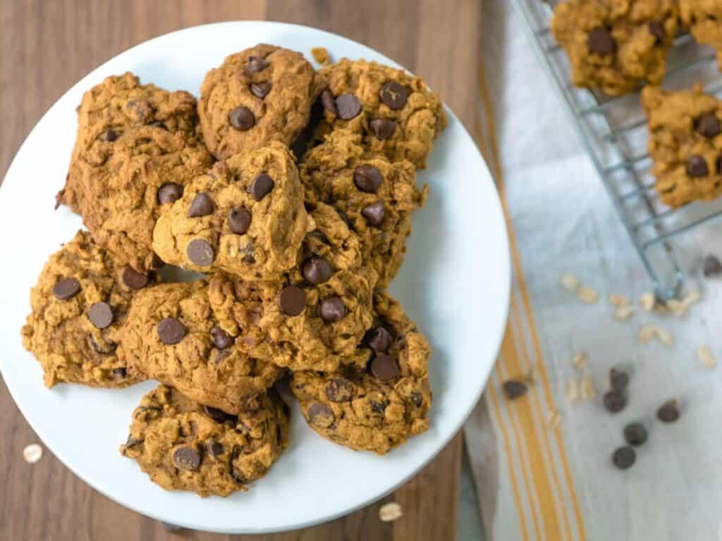 Image shows a bunch of pumpkin oatmeal chocolate chip cookies on a plate.