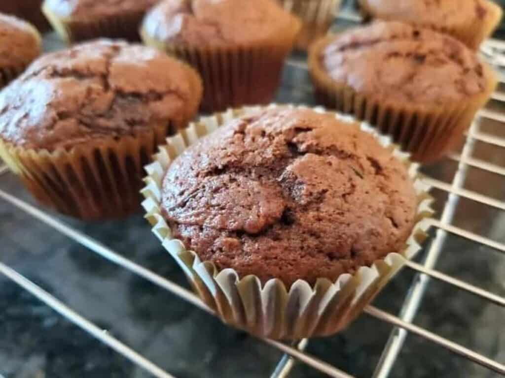 Image shows baked chocolate zucchini muffins on a wire cooling rack.