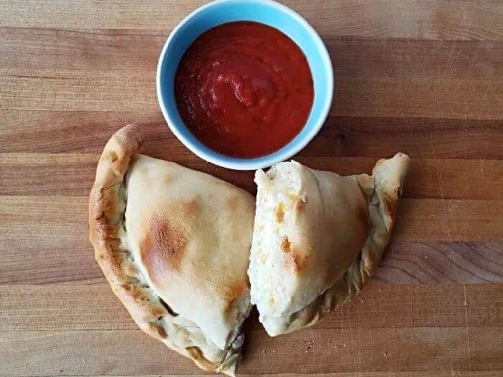 Image shows calzones with a small bowl of sauce.