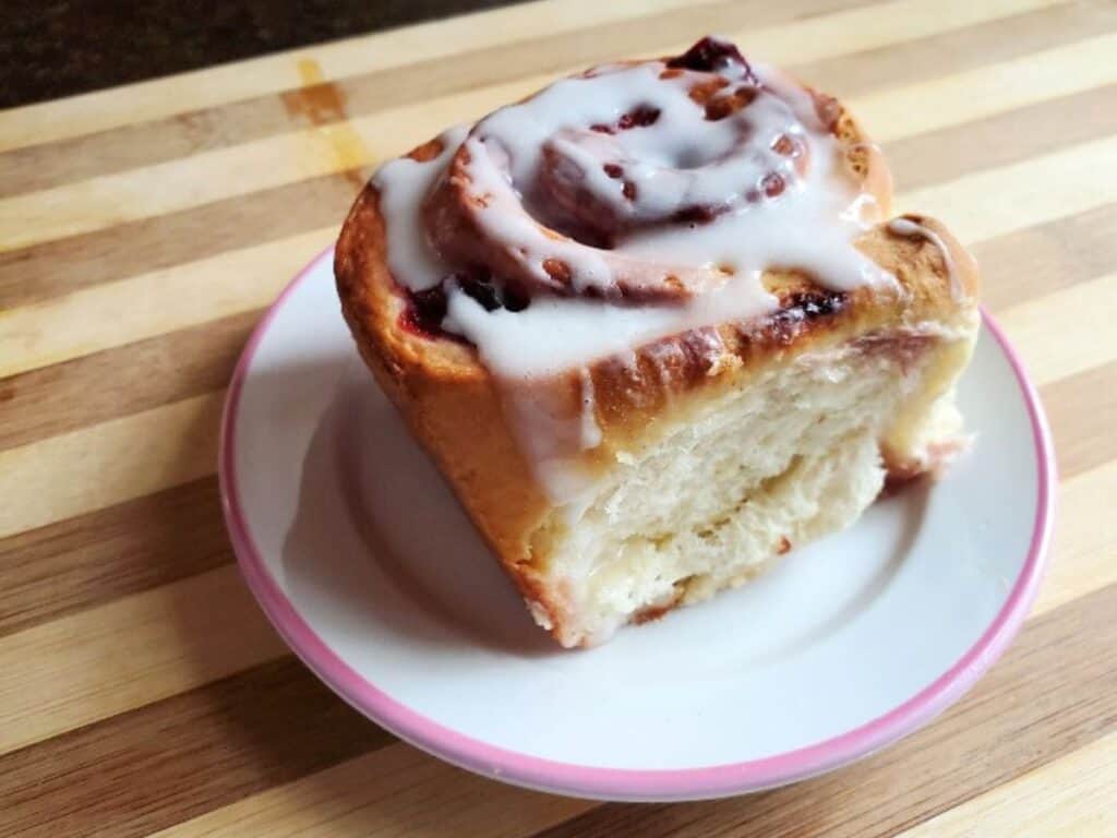 Image shows cherry cinnamon roll served on a plate.