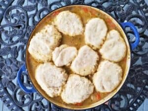 Image shows chicken stew with biscuits served in a pot.