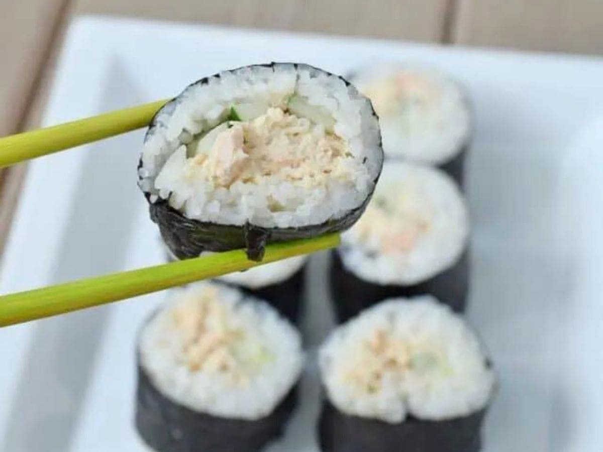 Image shows Chopsticks holding spicy tuna roll over a plate with more of the roll.