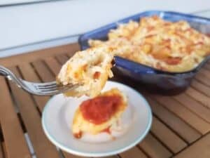Image shows close up picture of bite sized cheesy stuffed shell on a fork.