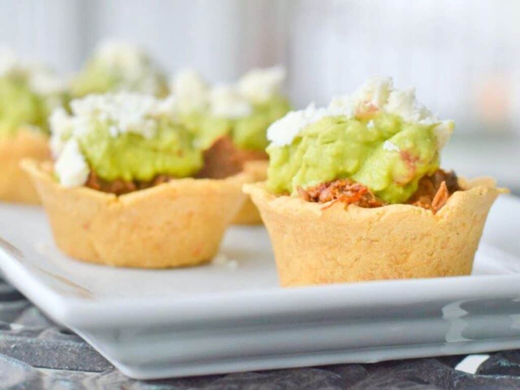 Image shows crockpot Mexican beef in masa cups on a serving plate.