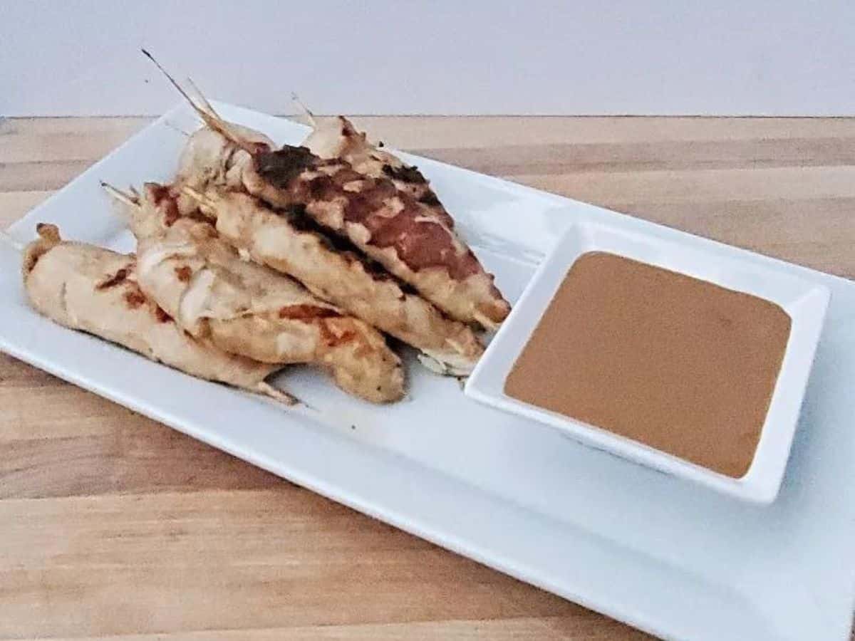 Chicken satay with peanut sauce on a white platter.