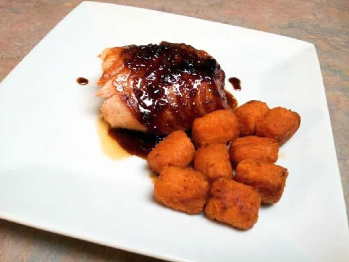 Image shows Soy ginger salmon on a white plate with sweet potato tater tots.