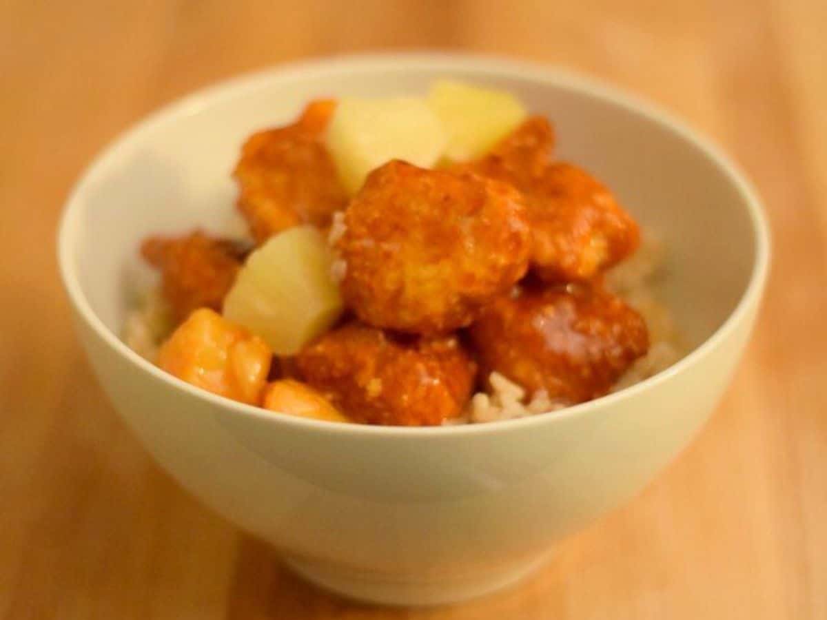 Image shows a Bowl of baked sweet and sour chicken with pineapple.