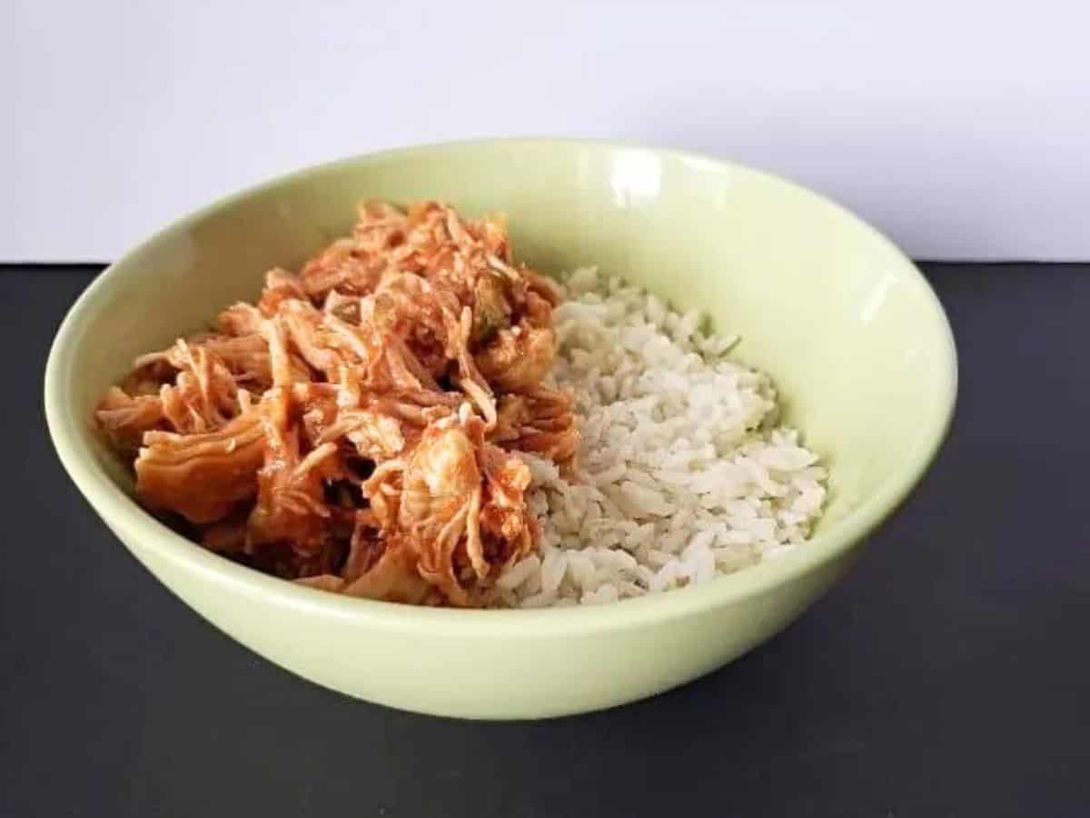 Image shows a Bite of tomato lime chicken on a fork with rice and the rest of the bowl in the background.