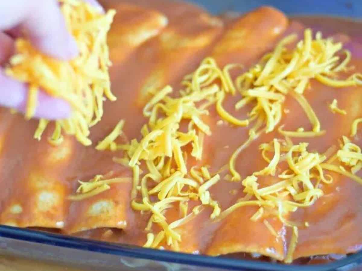 Image shows baked cheesy chicken enchiladas in a blue Pyrex casserole.