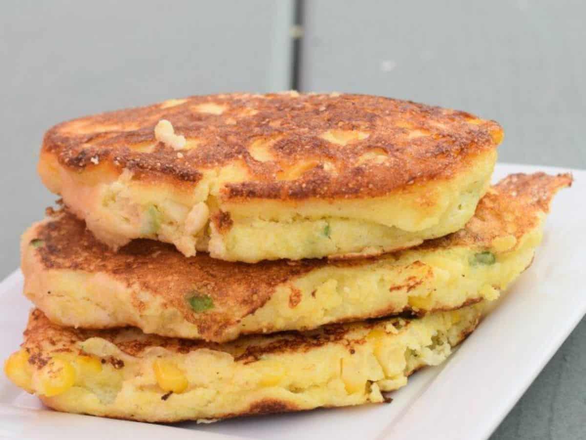 Image shows three corn fritters stacked atop each other on a white plate with a blue wooden background.