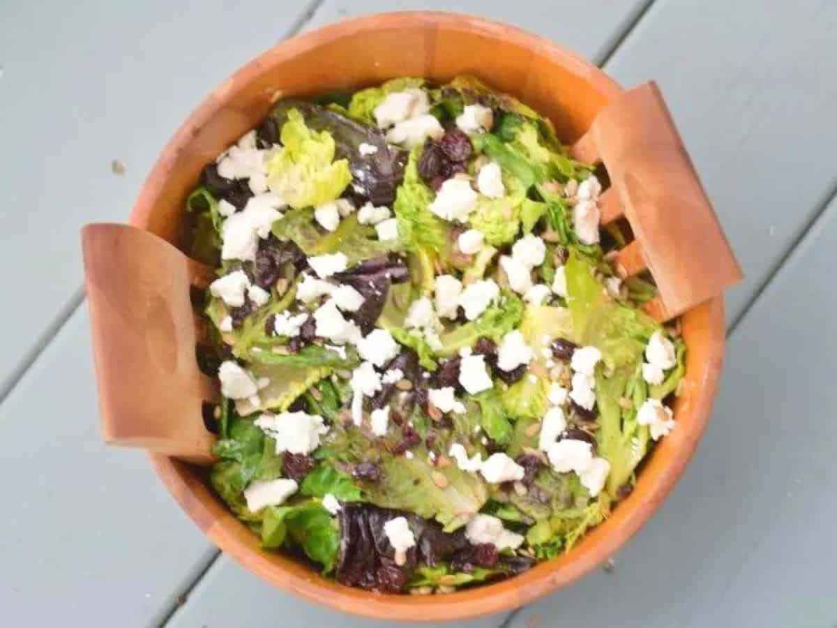 Image shows an overhead shot of a goat cheese and dried cherry salad in a wooden bowl.