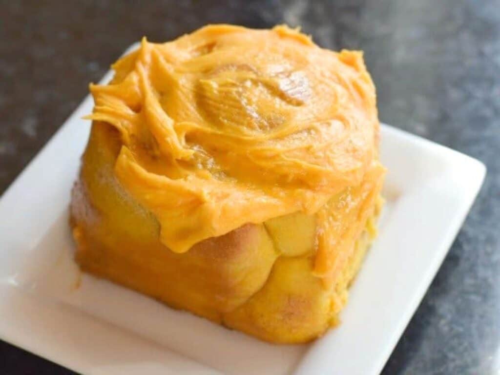 Image shows fresh pumpkin cinnamon roll served on a plate.