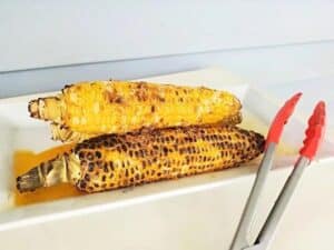 Image shows grilled corn served with tong.