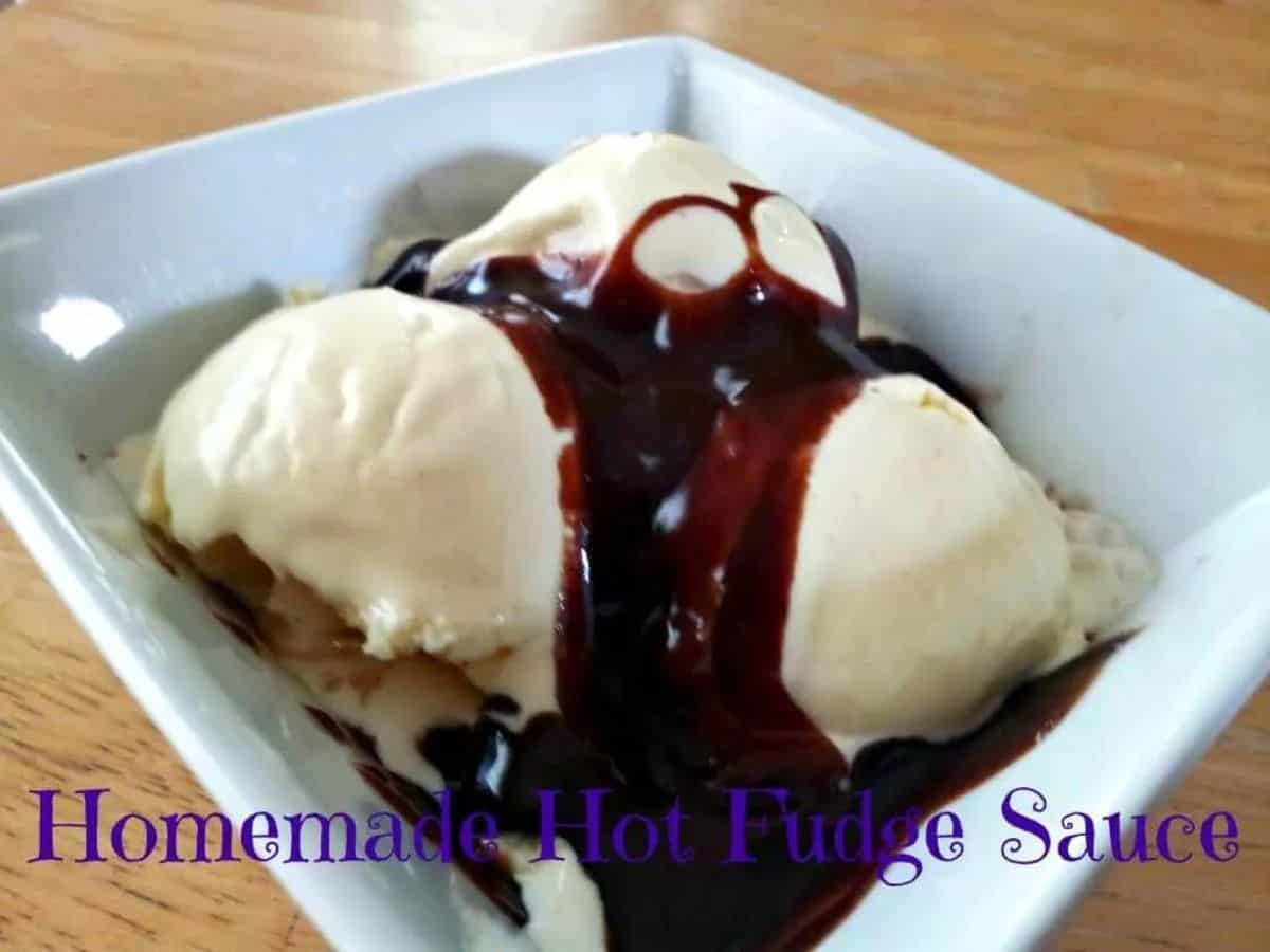 Image shows A bowl of vanilla ice cream topped with chocolate syrup on a wooden table.