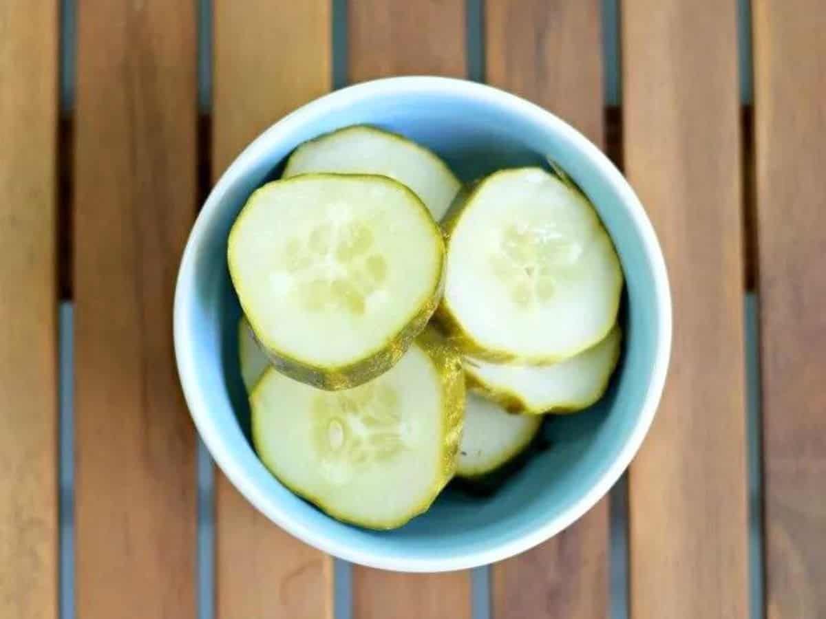 Image shows an overhead shot of sliced garlic dill pickles in a small dish sitting on a wooden board.