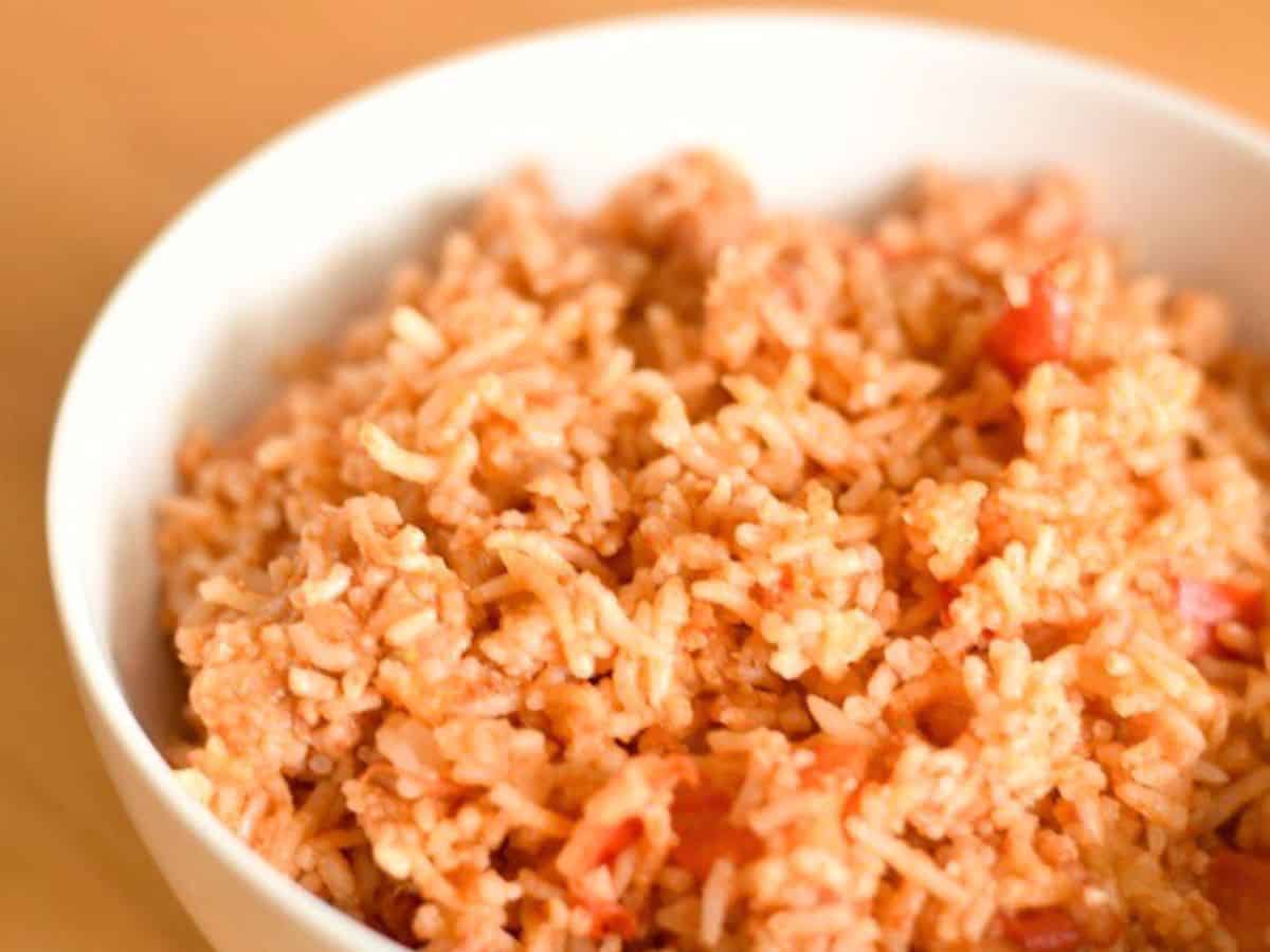 Overhead image of a white bowl containing Spanish rice sitting on a wooden board.