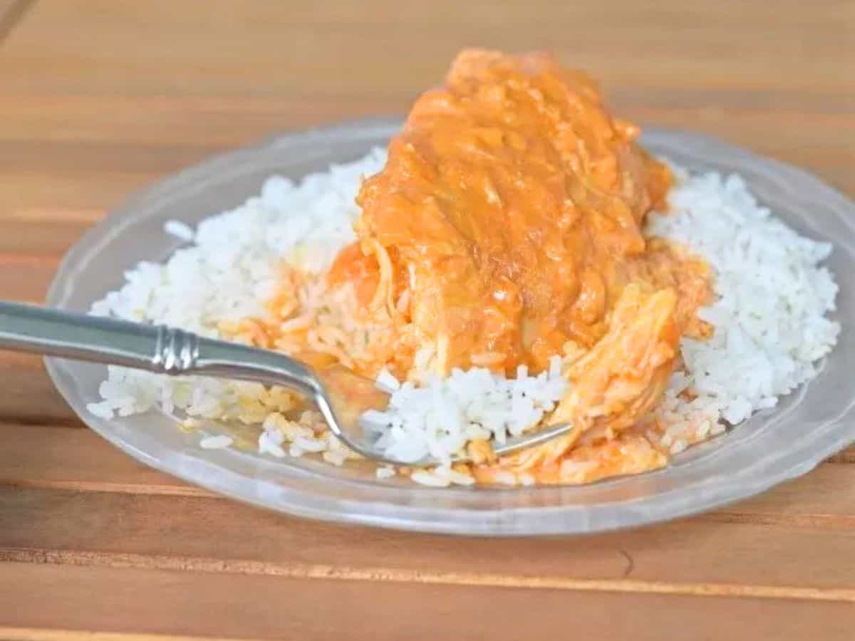 Image shows Bite of chicken paprikash on a fork sitting on a glass plate on a wooden table.