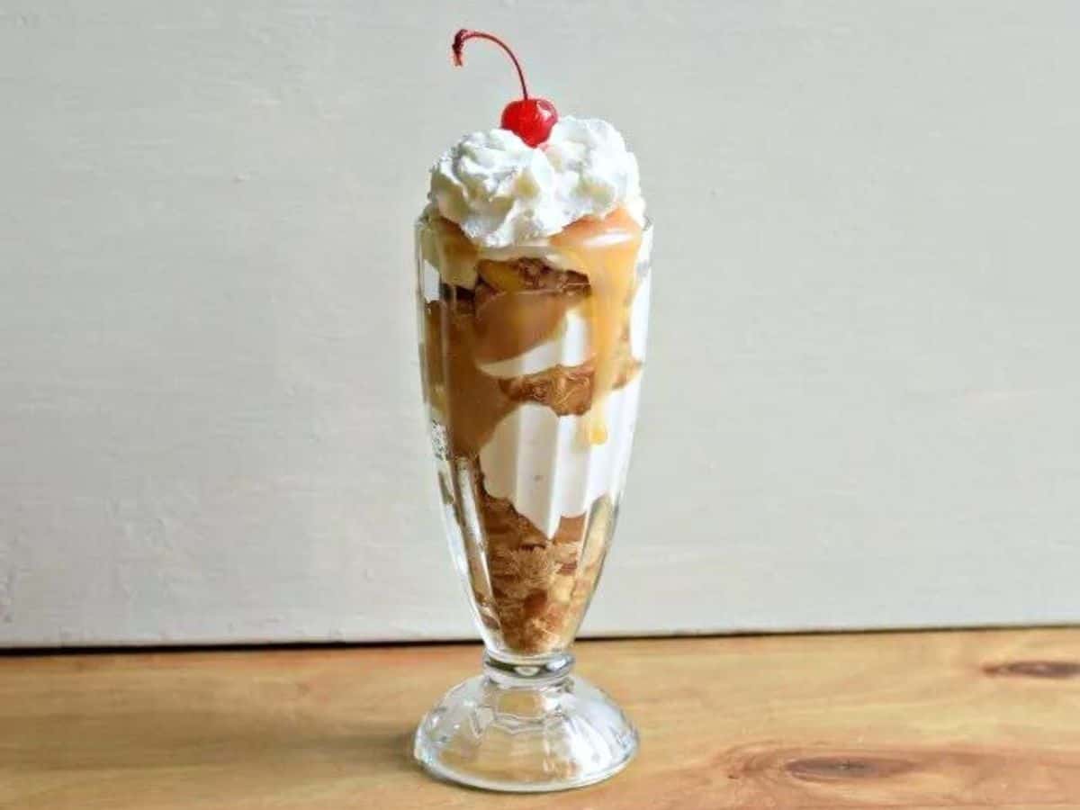 Image shows a close up of an Apple Pie Parfait in a milkshake glass topped with whipped cream and a cherry.