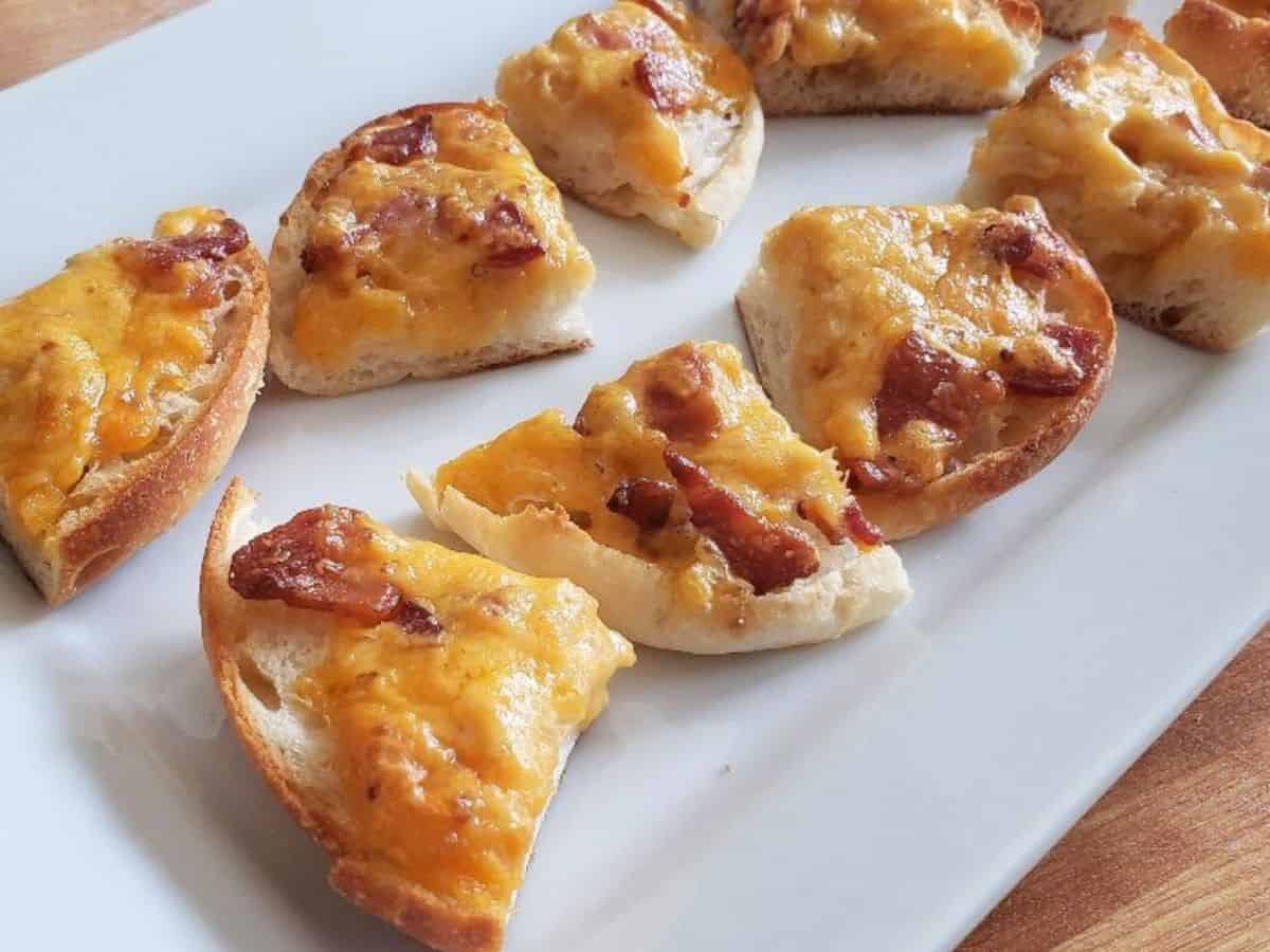 Image shows a hand holding a quarter of a Boozy Bacon Cheddar Bite with more on a white tray in the background.