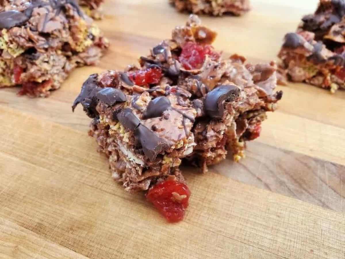 Photo shows a double chocolate cherry cereal bar on a wooden board with more in the background.