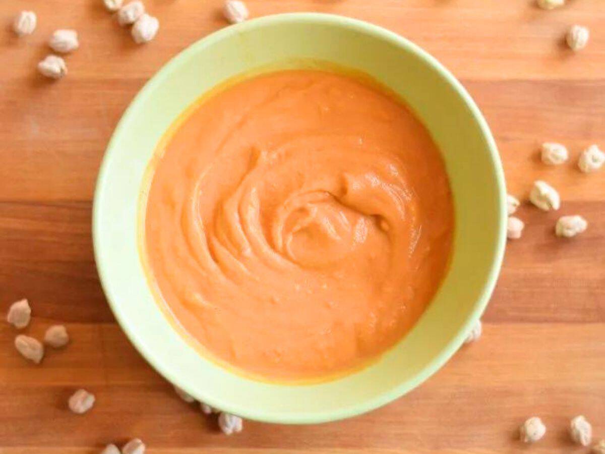 Image shows A bowl of creamy chickpea tomato soup with dried chickpeas around it.