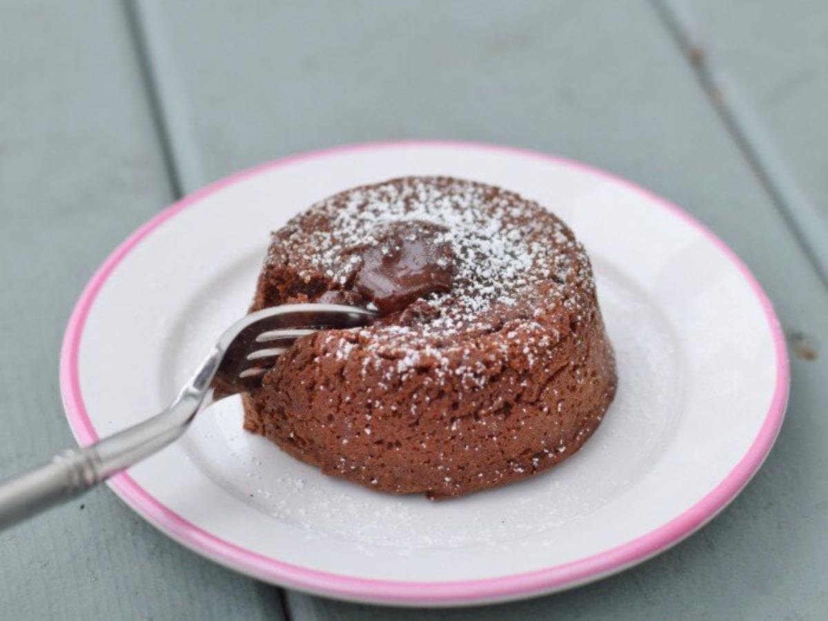 Image shows a fork pulling a bite from a molten chocolate cake on a white plate.