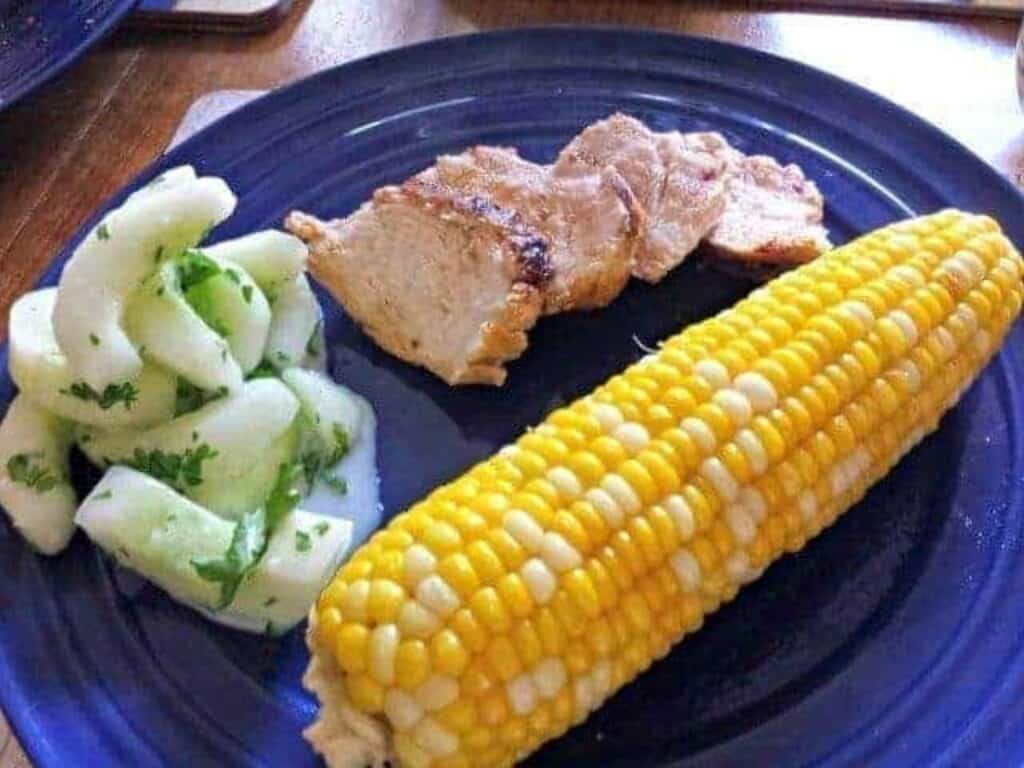 Image shows lemon marinated kefir chicken served with cucumber salad and corn.
