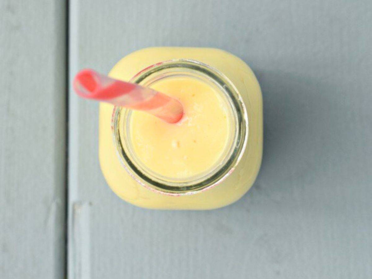 Image shows an overhead closeup image of a Mango Lassi in a glass jar with a straw in it.