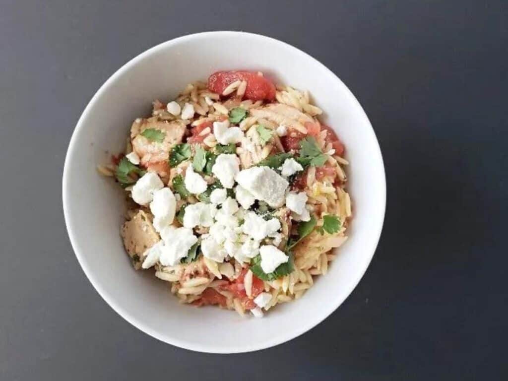 Image shows Mediterranean chicken with orzo in a bowl.