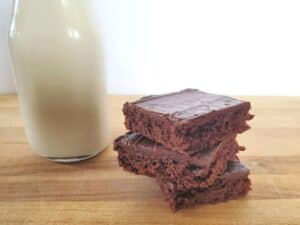 Image shows Mexican sheetcake brownies stacked with a glass of milk at the back.