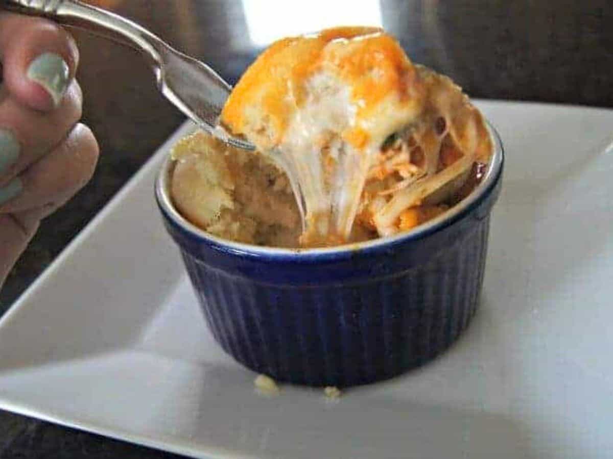 Image shows a fork with a great cheese pull taking a bite from a blue ramekin containing a chicken pizza pot pie.