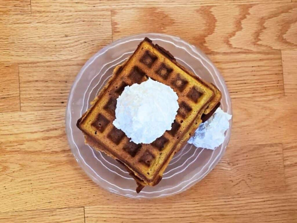 Image shows pumpkin waffle served on a plate with whipped cream.