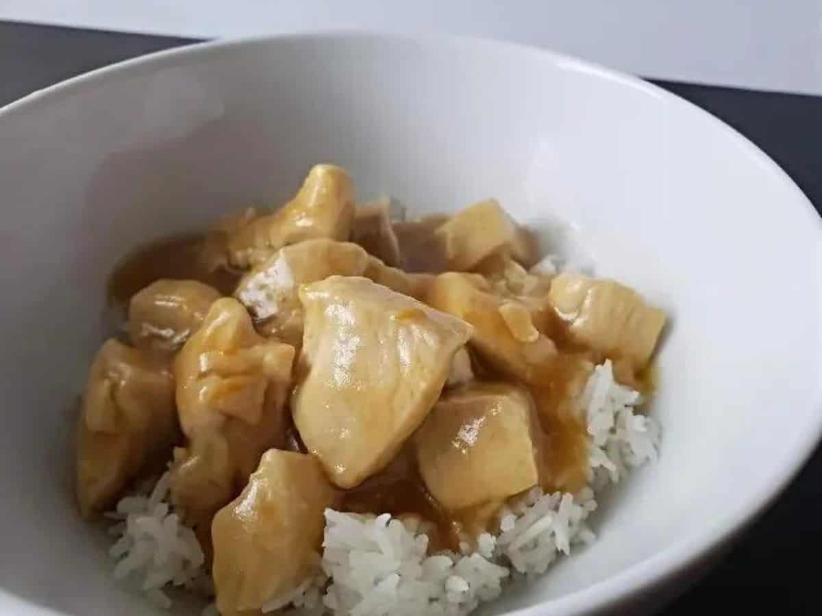 Image shows a Fork holding orange chicken with rice with the full bowl behind it.