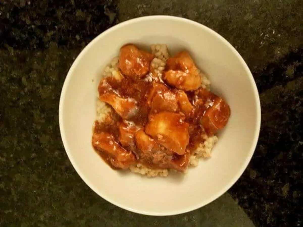 Overhead shot of honey bourbon chicken in a bowl on a black counter.