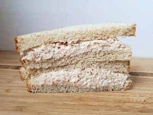 Image shows shortcut chicken salad sandwich cut in half sitting on a wooden table.