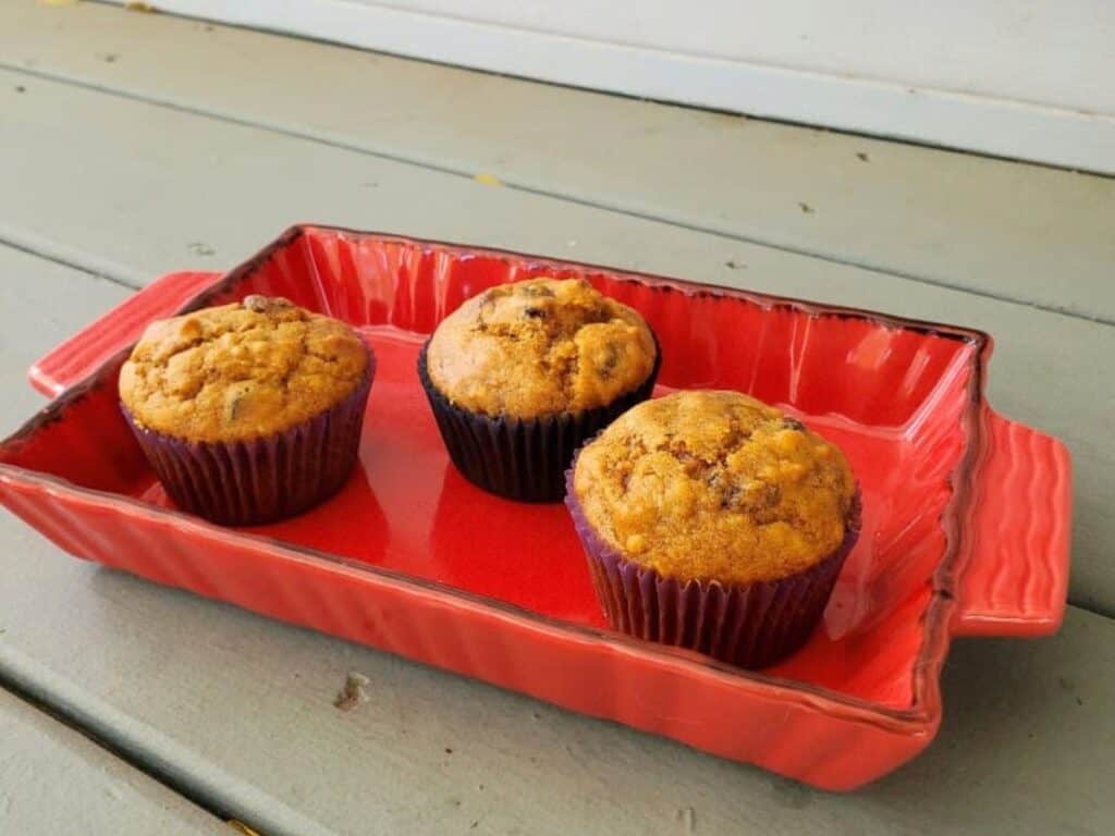 Image shows three cranberry pumpkin muffins in a red tray.