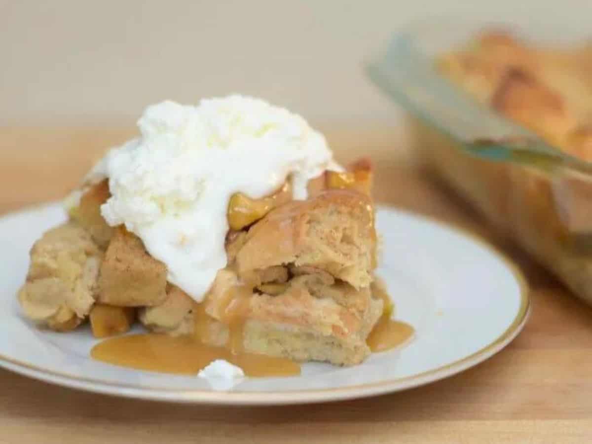 Image shows a head on close up shot of a slice of Apple Pie Bread Pudding topped with whipped cream.