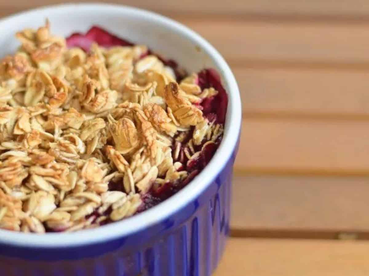Image shows A spoon lifting berry oatmeal from a ramekin, showcasing the juicy fruit topping and golden-brown crust beneath.