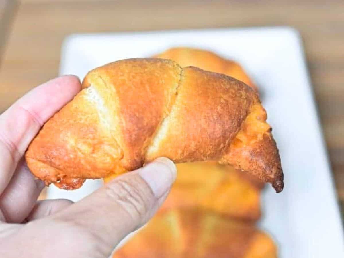Image shows A person holding a buffalo chicken roll over a plate filled with more.